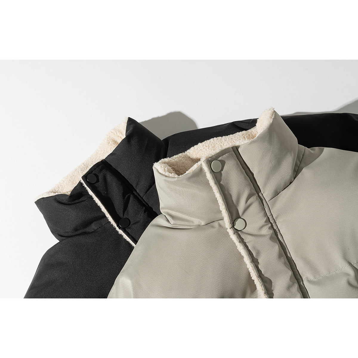 Close-up of black and light gray padded jackets showing cream fleece lining and snap-button collars.