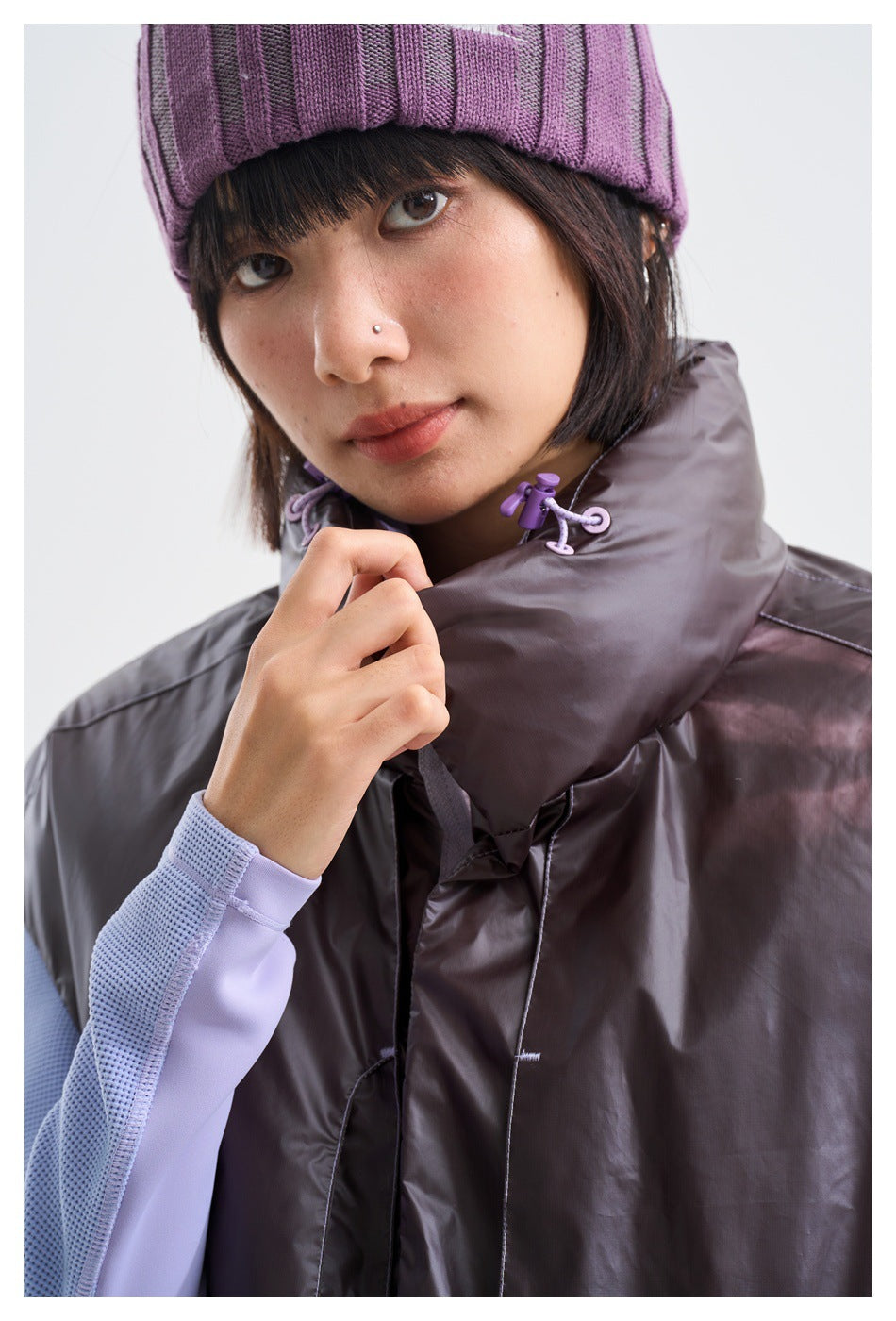 Close-up of a model wearing a charcoal-gray vest with a high collar and purple drawcord toggles.
