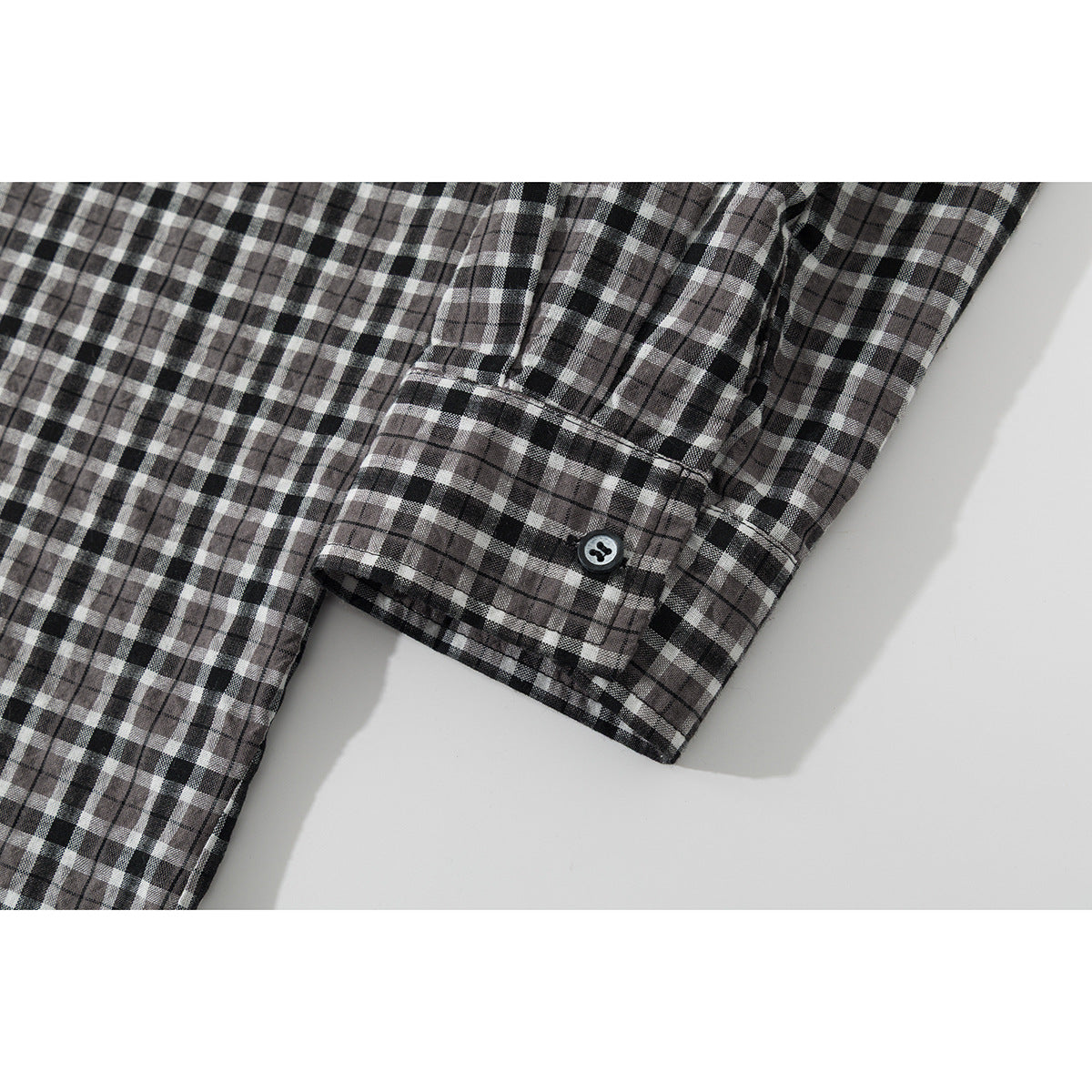 Close-up of the plaid shirt's long sleeve and buttoned cuff against a white background.