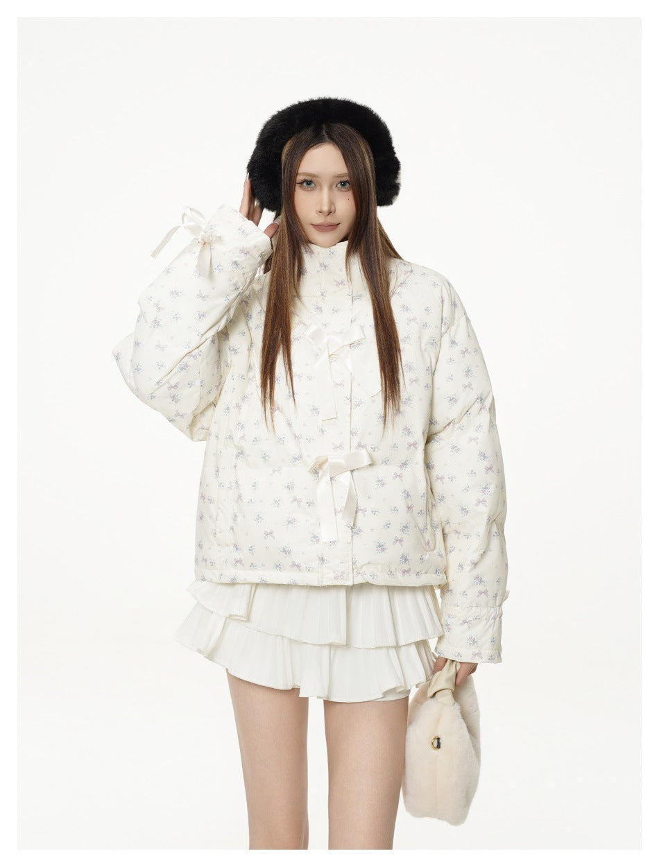 Model with a raised arm wearing a cream floral-print quilted jacket with satin bows and cuff ribbon ties
