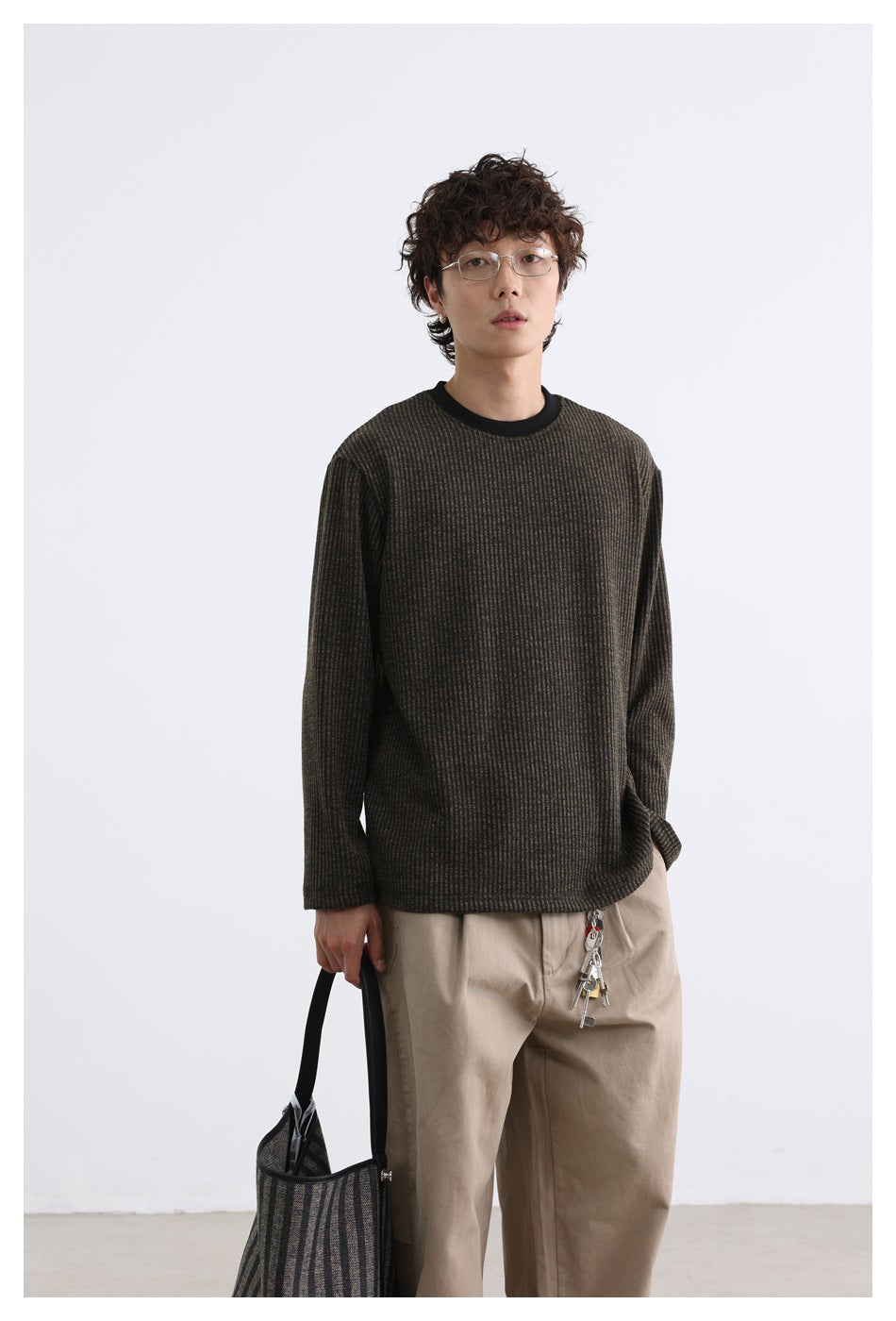 Model wearing a dark brown subtly striped long-sleeve shirt with a black crew neck, paired with beige trousers.