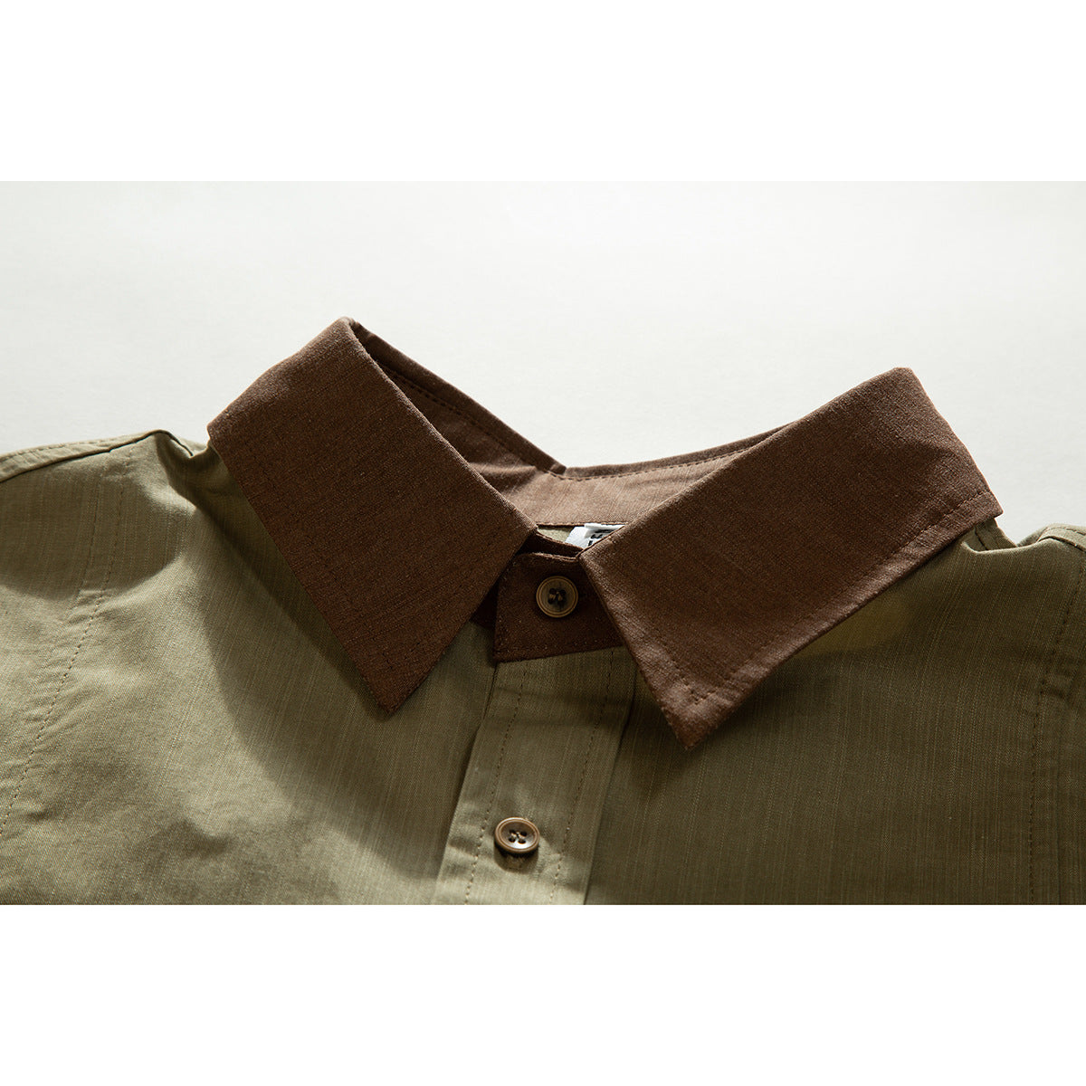 Close-up of an olive shirt with a contrasting brown pointed collar and brown buttons.