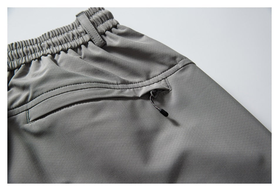 Close-up of gray trousers showing an elastic waistband and curved zip pocket with a pull cord.