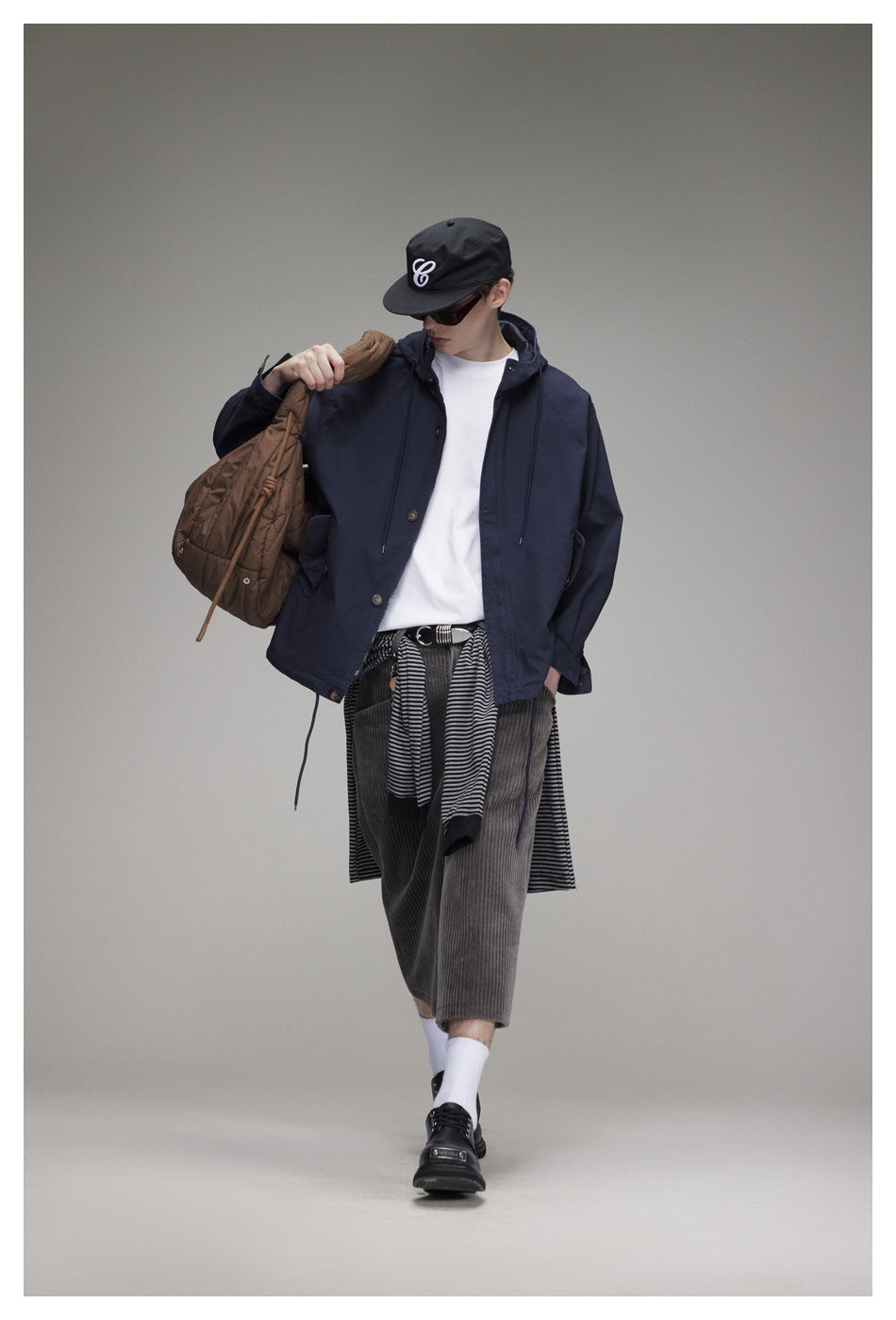 Full-length model wearing a navy hooded jacket, white T-shirt, and gray cropped trousers.