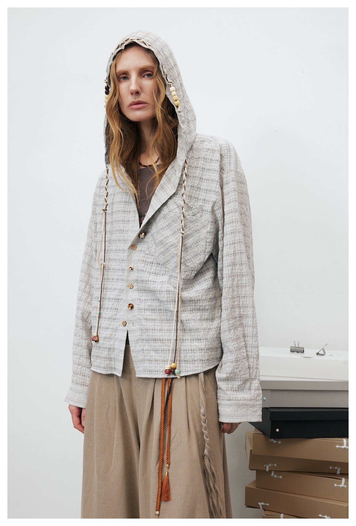 Model wearing a light gray checked hooded jacket with braided drawcords, colorful beads, and flower-shaped buttons.