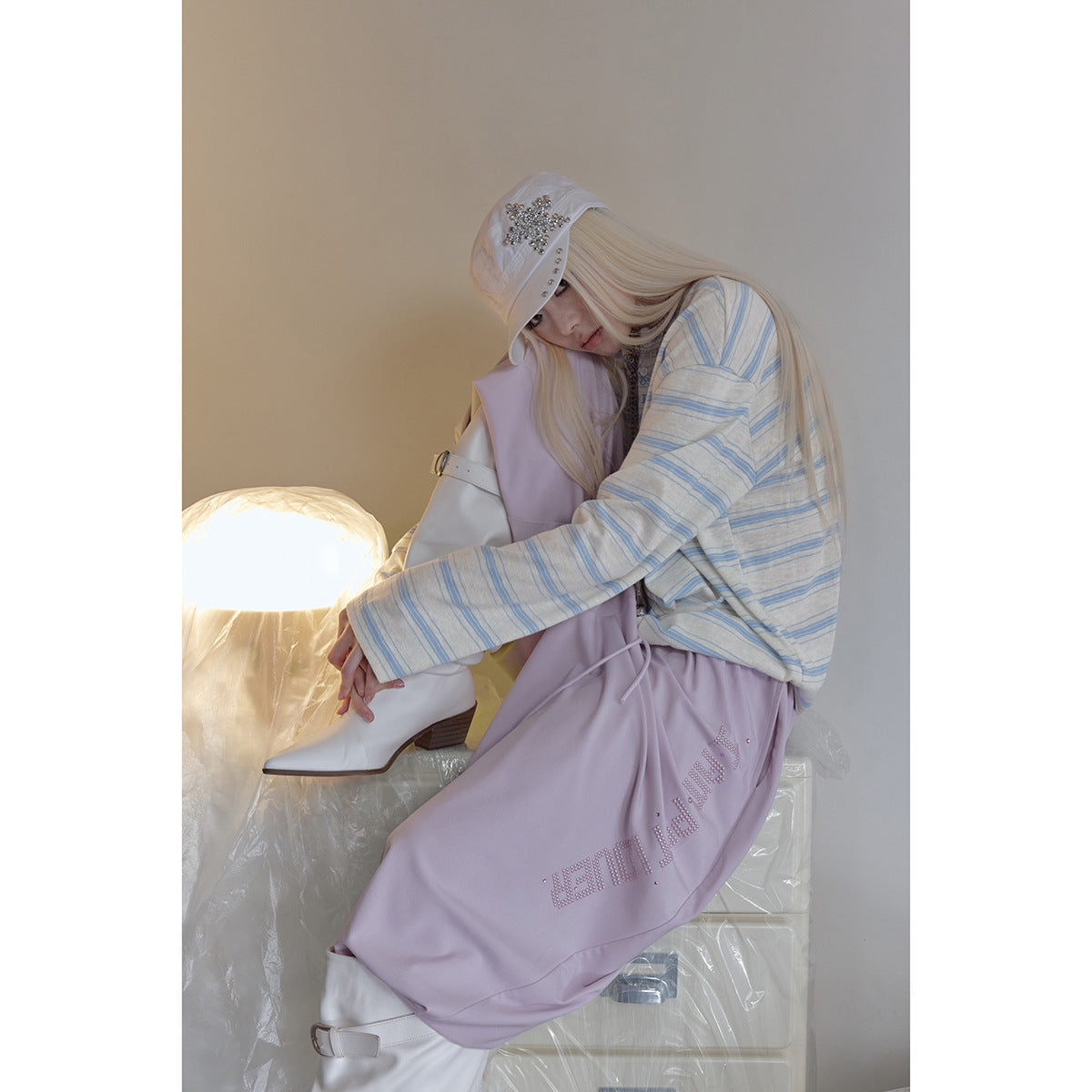 Seated model wearing a cream-and-blue striped top and loose lavender pants with rhinestone lettering.