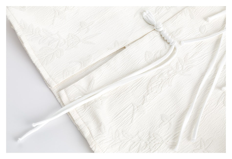 White braided drawstring and long ties lie across overlapping floral-textured fabric panels.