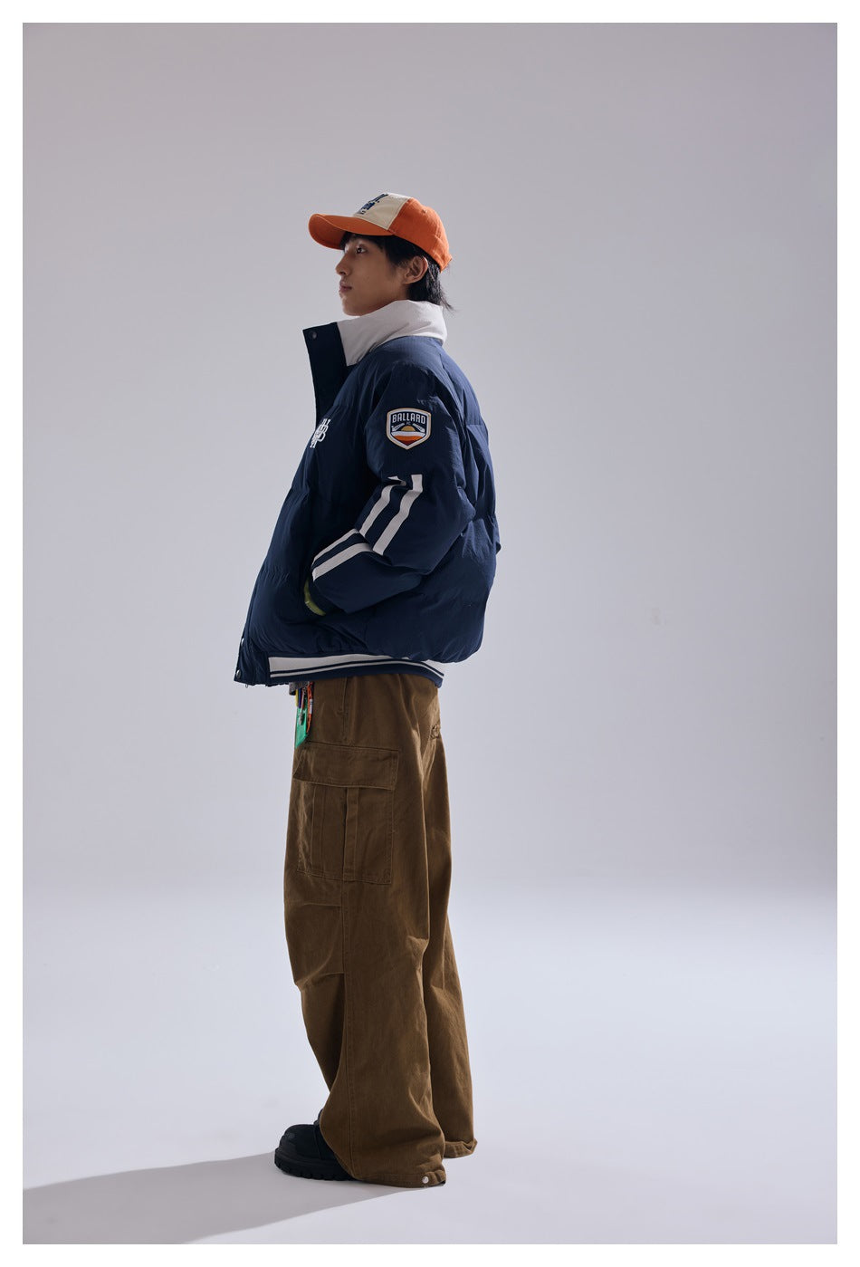 Side view of a model wearing a navy padded jacket with white sleeve stripes and a sleeve patch, with brown cargo pants.