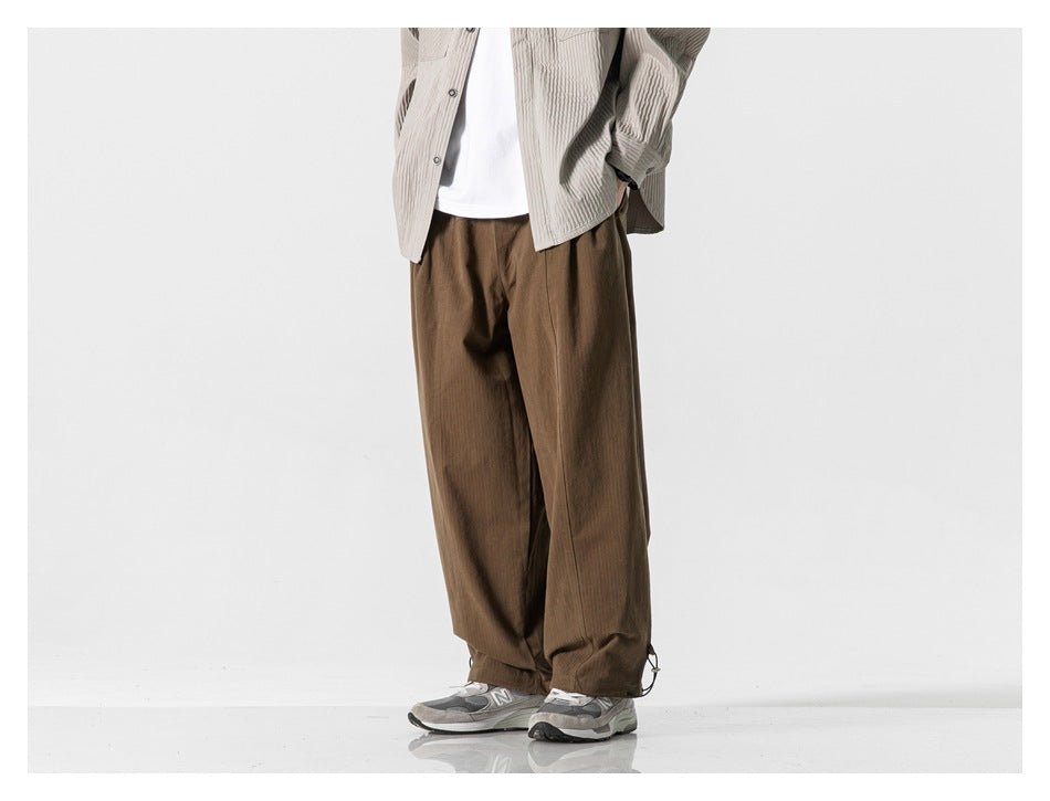 Model wearing loose brown trousers, shown from a slight front angle with drawcord hems.