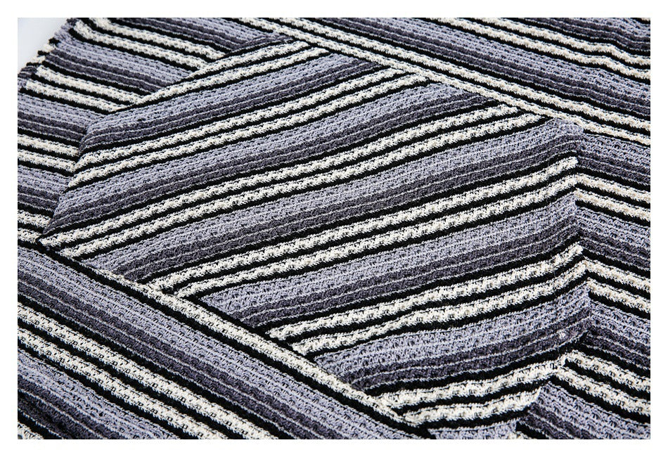 Close-up of folded black, charcoal, and ivory striped open-knit fabric with overlapping edges.
