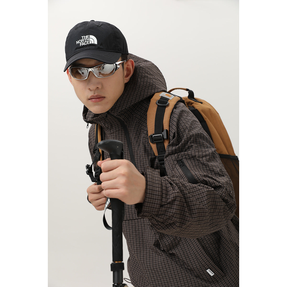 Close view of a model in a dark brown checked hooded jacket, showing its sleeve pocket and fabric pattern.