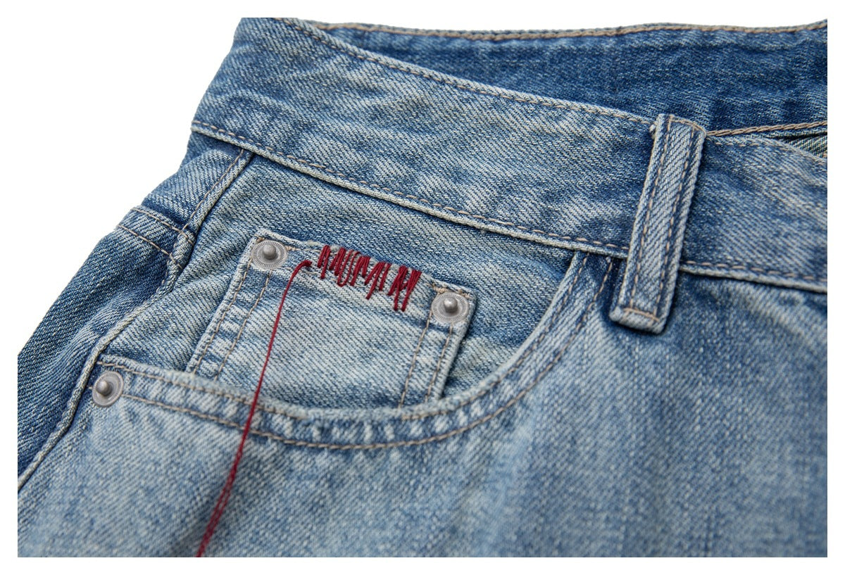 Close-up of a front pocket on light blue denim shorts with red embroidered stitching.