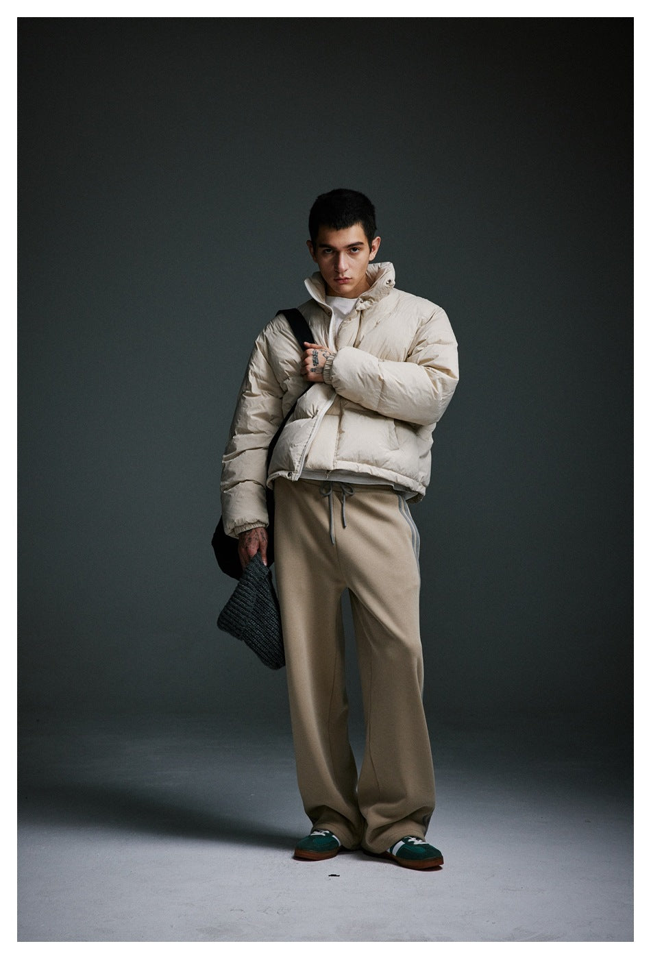 Model wearing a cream puffer jacket and loose taupe drawstring pants with green sneakers.