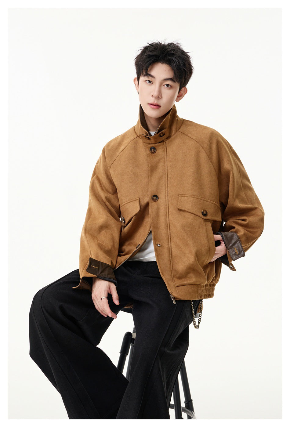 Seated model wearing a tan-brown button-front jacket with dark collar and cuff accents.