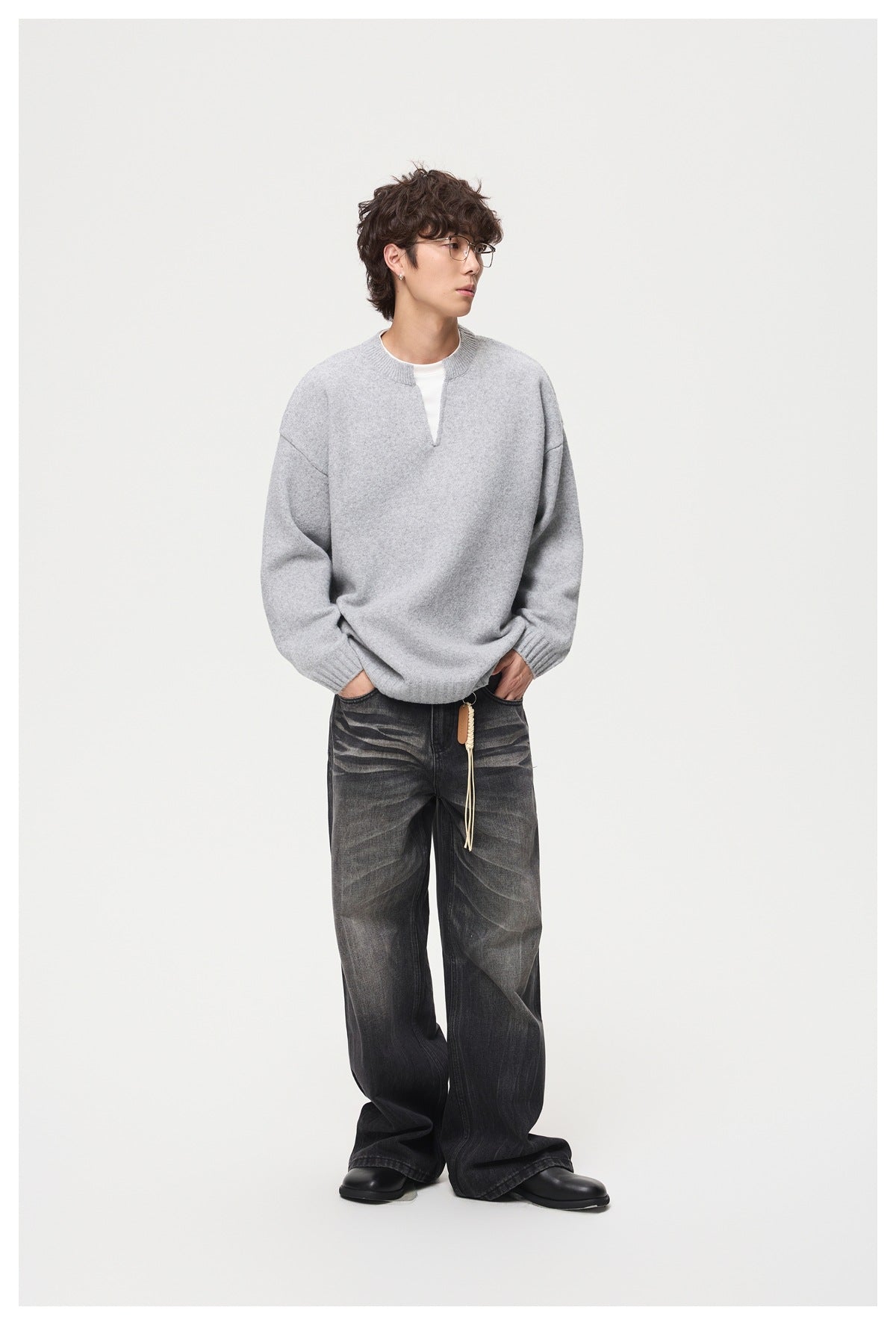 Man wearing a light gray oversized knit sweater over a white top with faded black wide-leg jeans, hands in pockets