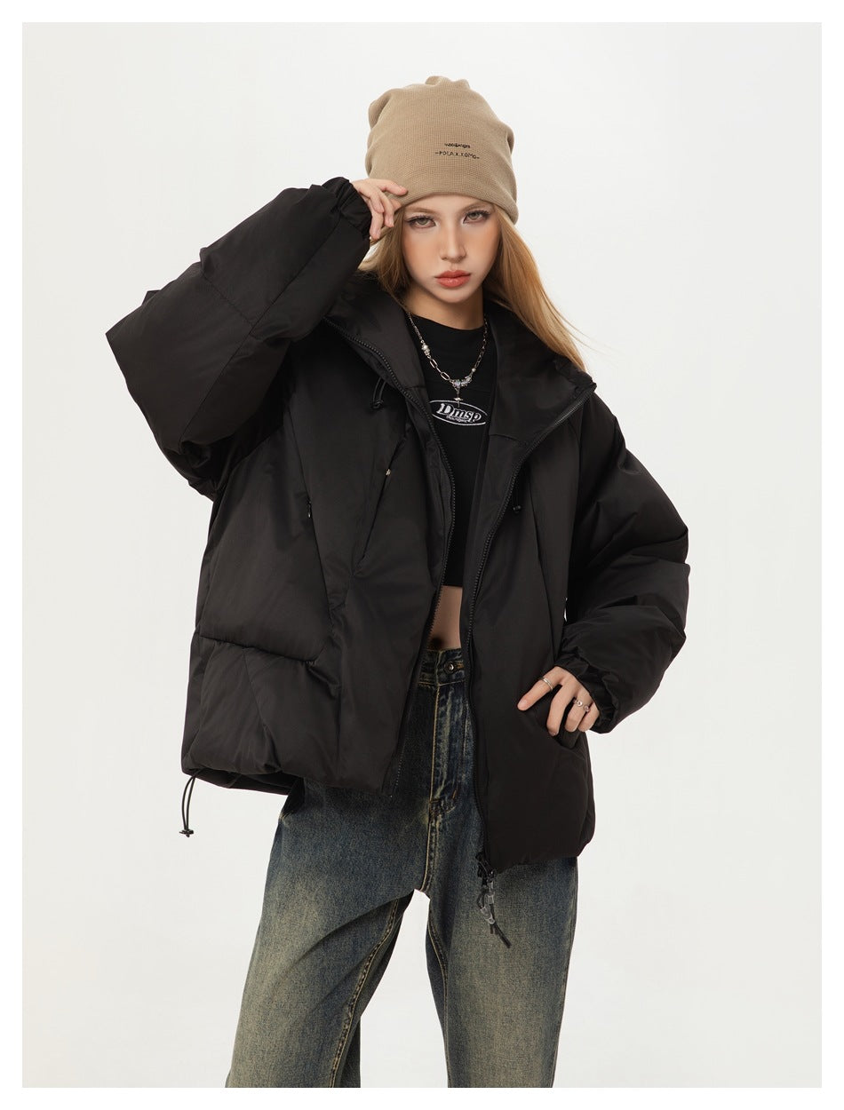 Model posing in a black puffer jacket and beige beanie, with the jacket worn open over a black top.