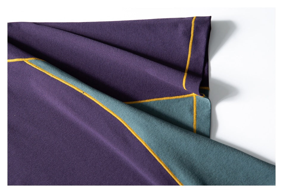 Folded purple garment showing a teal panel and mustard-yellow contrast seams on a white surface.