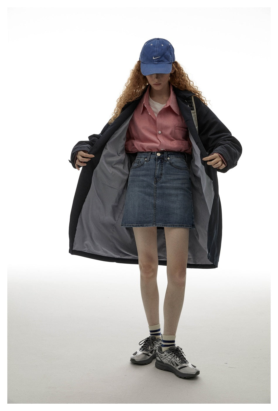 Model opens a dark navy coat to show its gray lining, layered over a pink shirt and denim skirt.