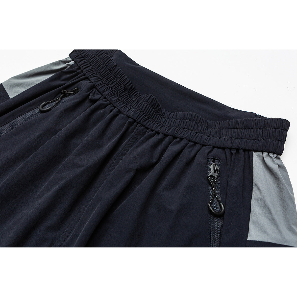 Close-up of navy pants with an elastic waistband, zip pockets and gray contrast panels.