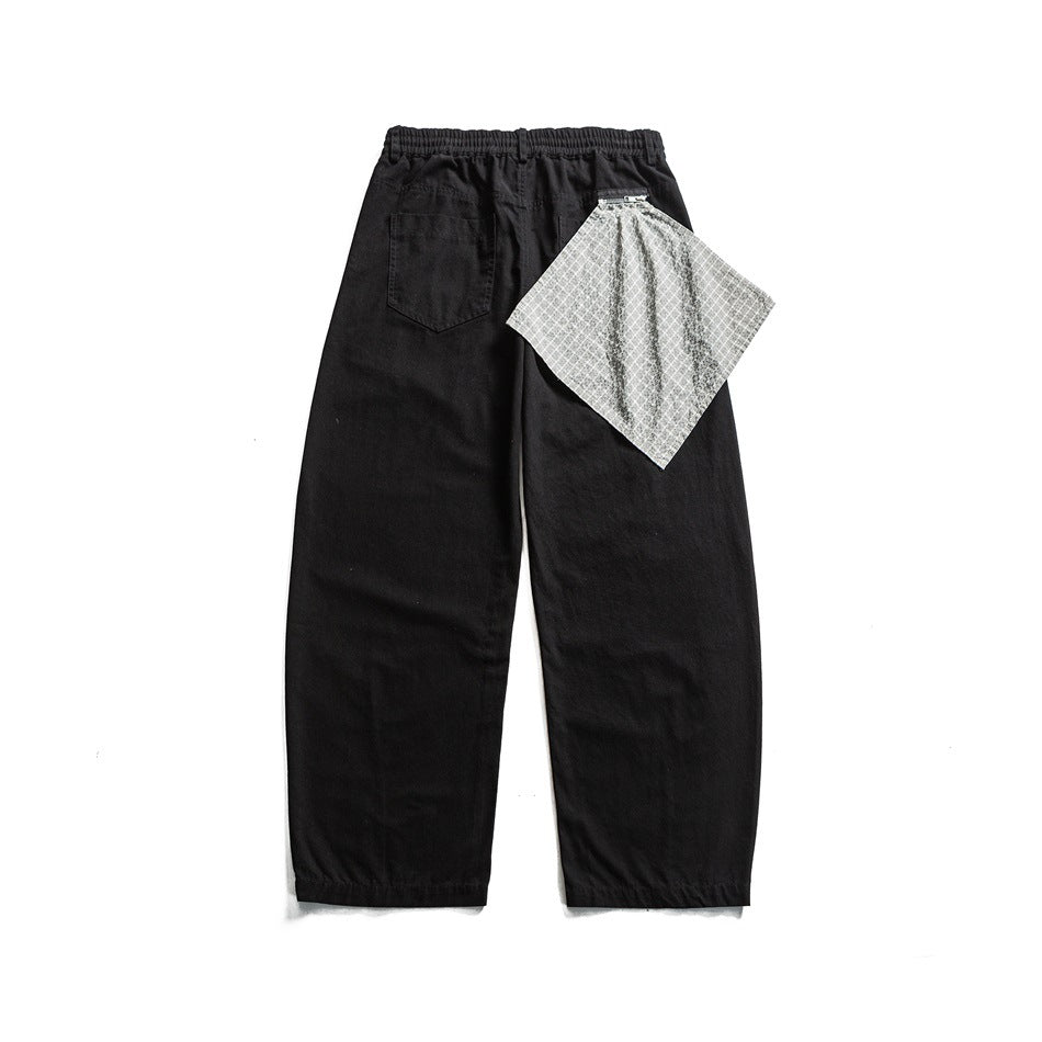 Back view of black wide-leg pants with elastic waistband, back patch pocket and gray checked cloth hanging at the waist