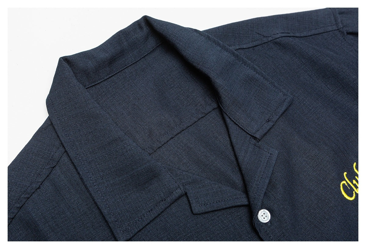Close-up of a dark navy short-sleeve shirt collar and button placket, with a glimpse of yellow embroidery.