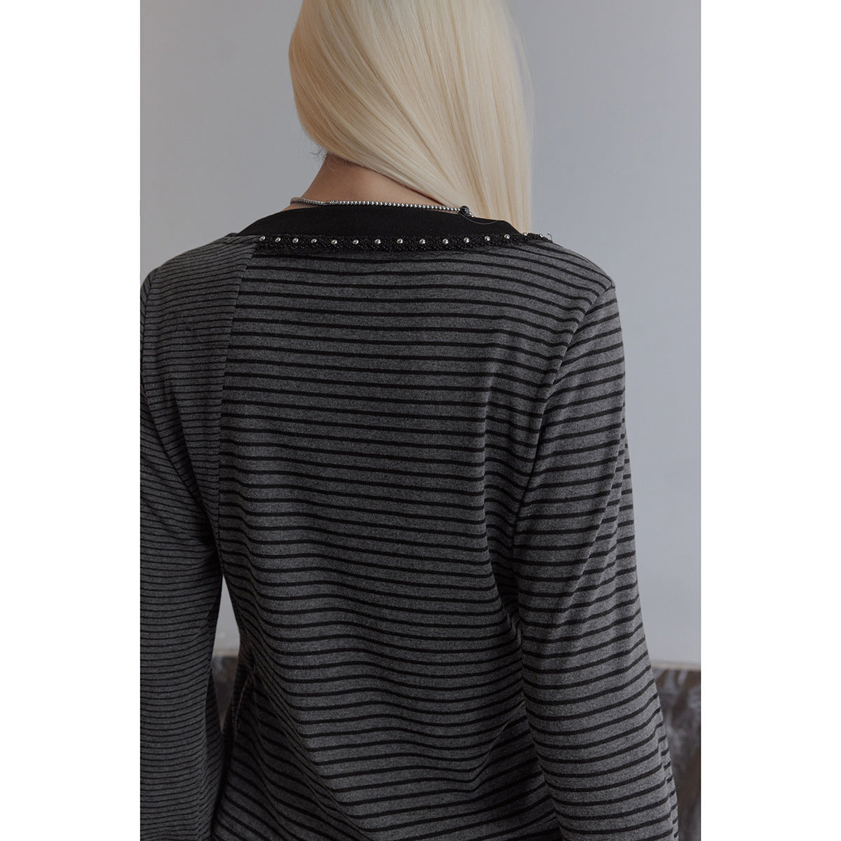 Close back view of a charcoal top with thin black stripes and stud trim along the neckline, worn by a model.