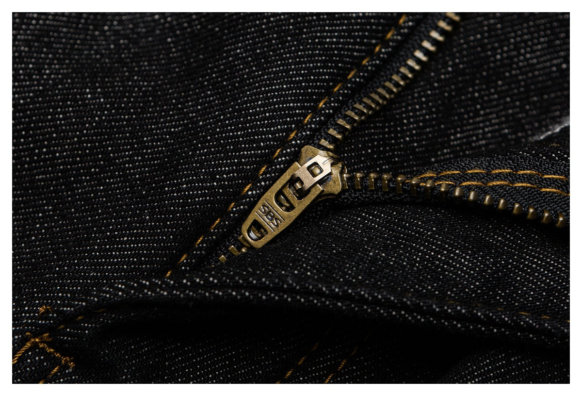 Macro close-up of a brass-colored jeans zipper on black denim with golden-brown stitching.