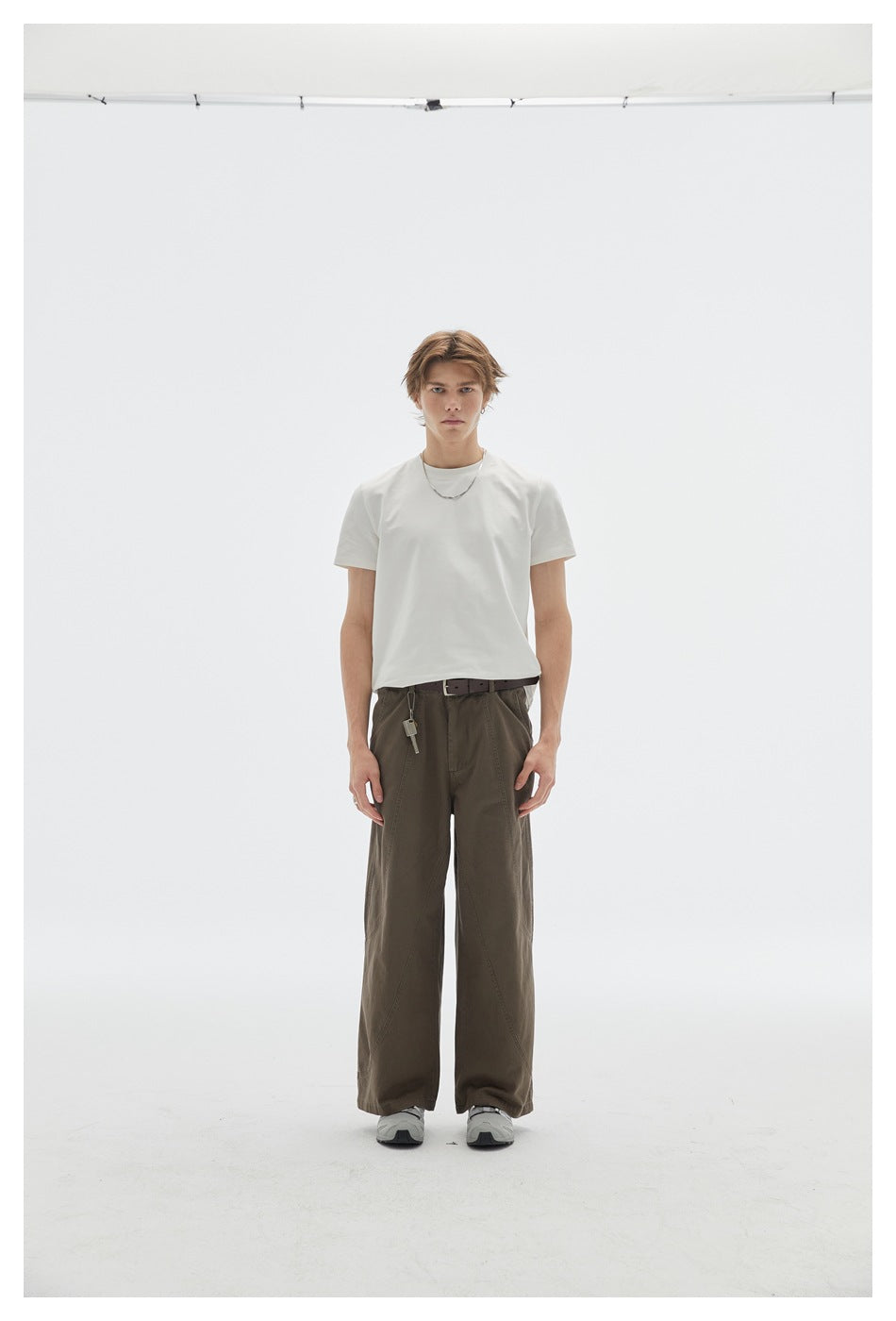 Front view of a model in a plain white T-shirt and dark olive wide-leg trousers with gray sneakers.