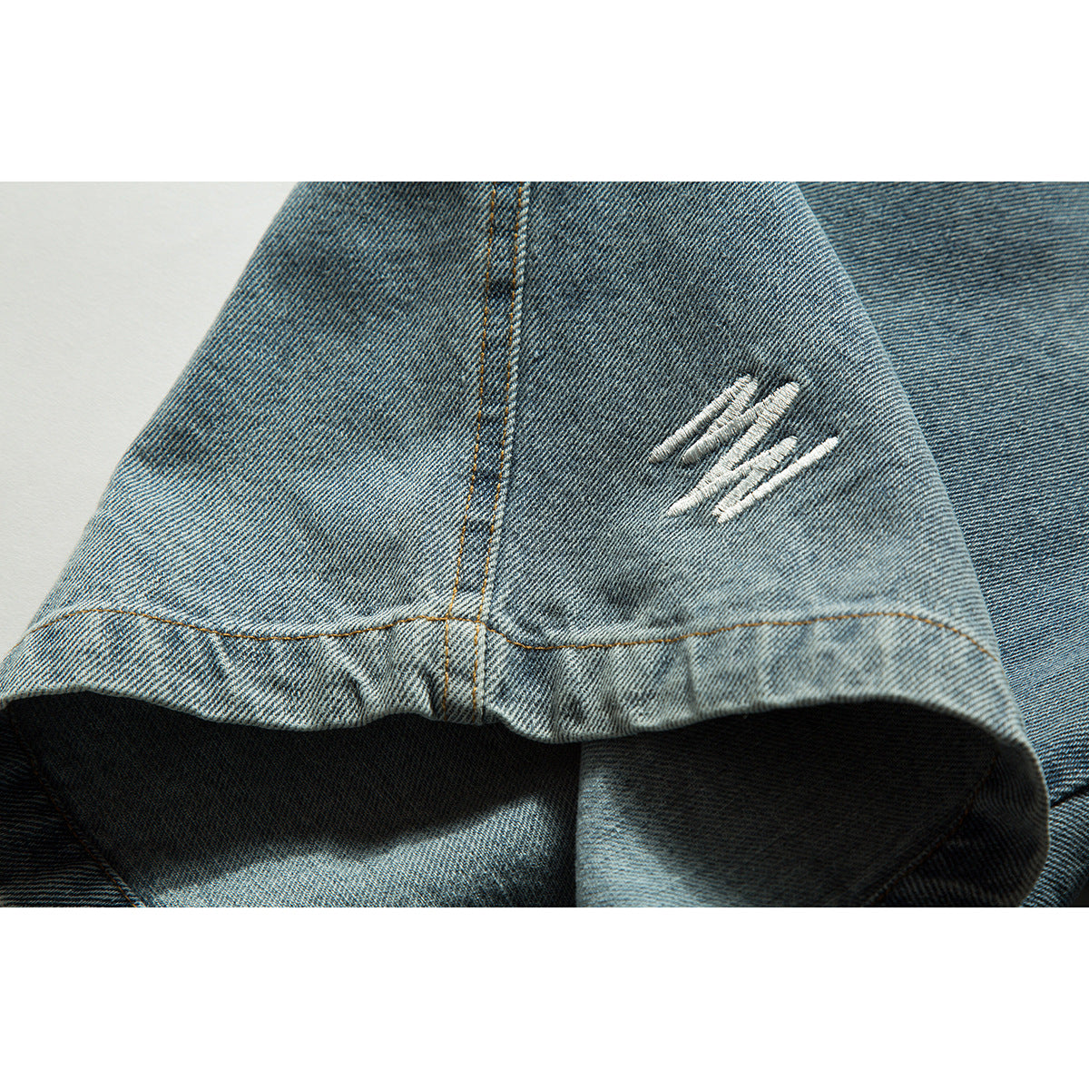 Close-up of a blue denim shorts hem with a small white stitched motif and contrasting seam.