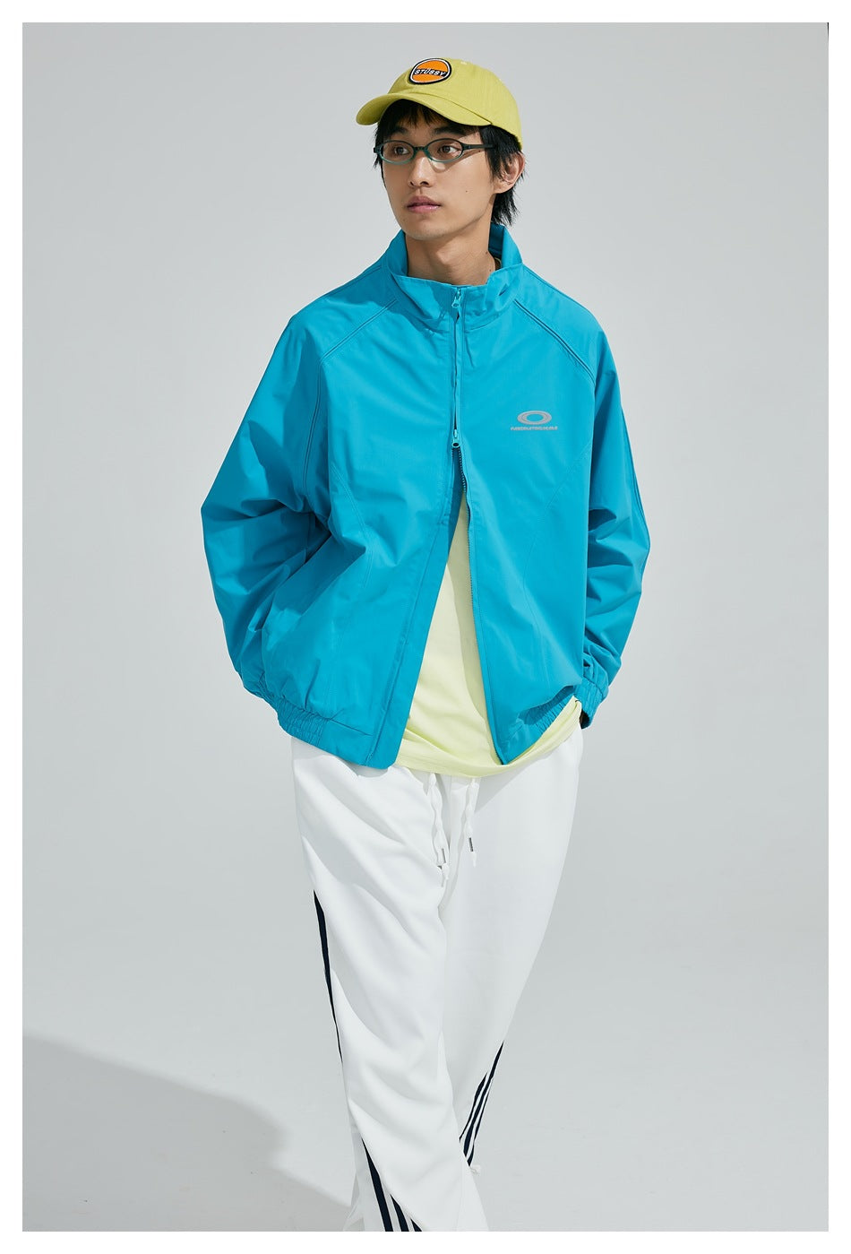 Model wearing a turquoise high-collar zip-up jacket with elastic cuffs and hem, shown from the front.