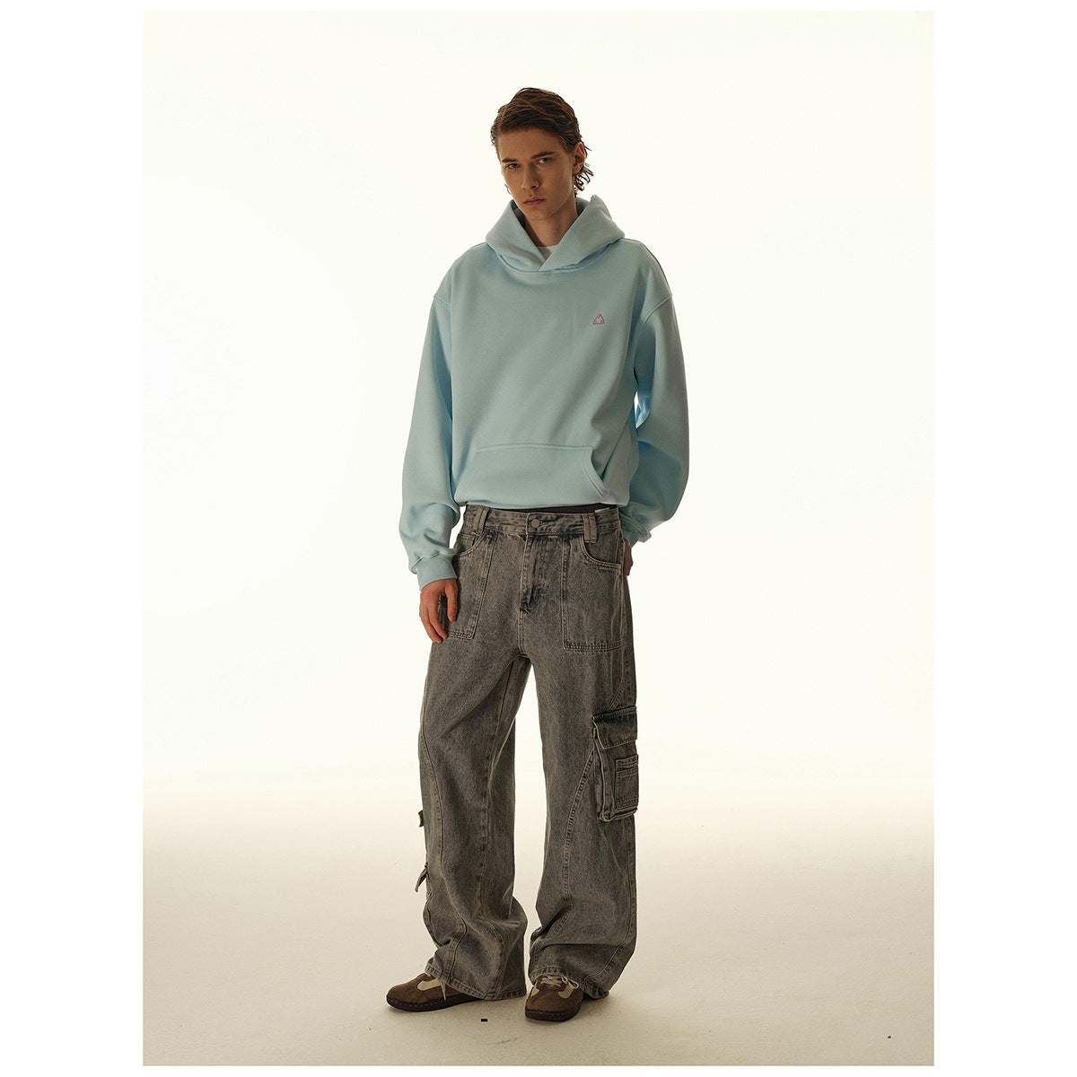 Full-length front view of a model wearing a light blue pullover hoodie and loose gray cargo jeans.