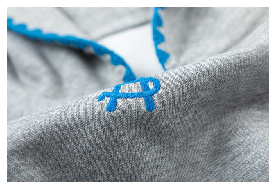 Close-up of a small blue embroidered emblem on heather gray fabric, with blue edge trim behind it.