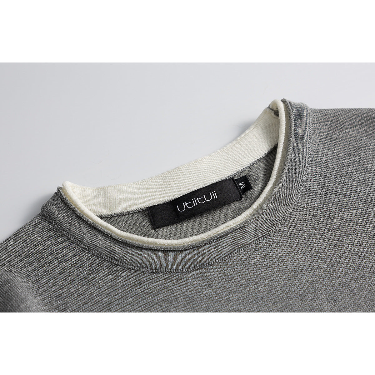Close-up of a gray knit shirt's crew neckline with cream contrast trim and a black neck label.