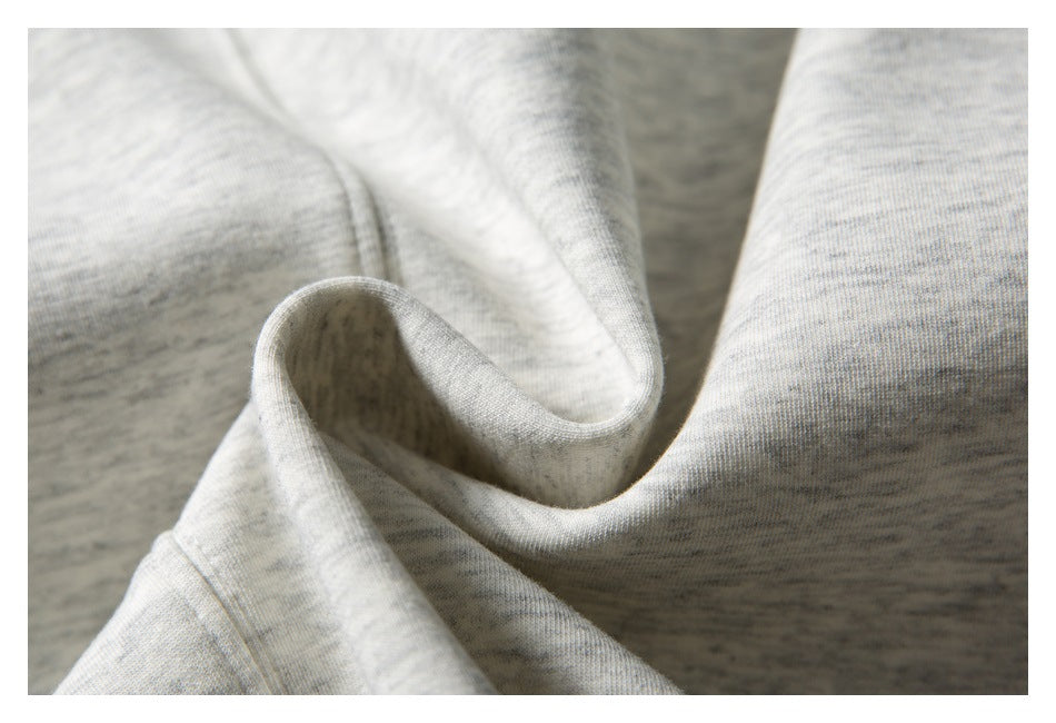 Close-up of light gray heathered fabric gathered in folds, showing its fine surface texture and stitched edge.