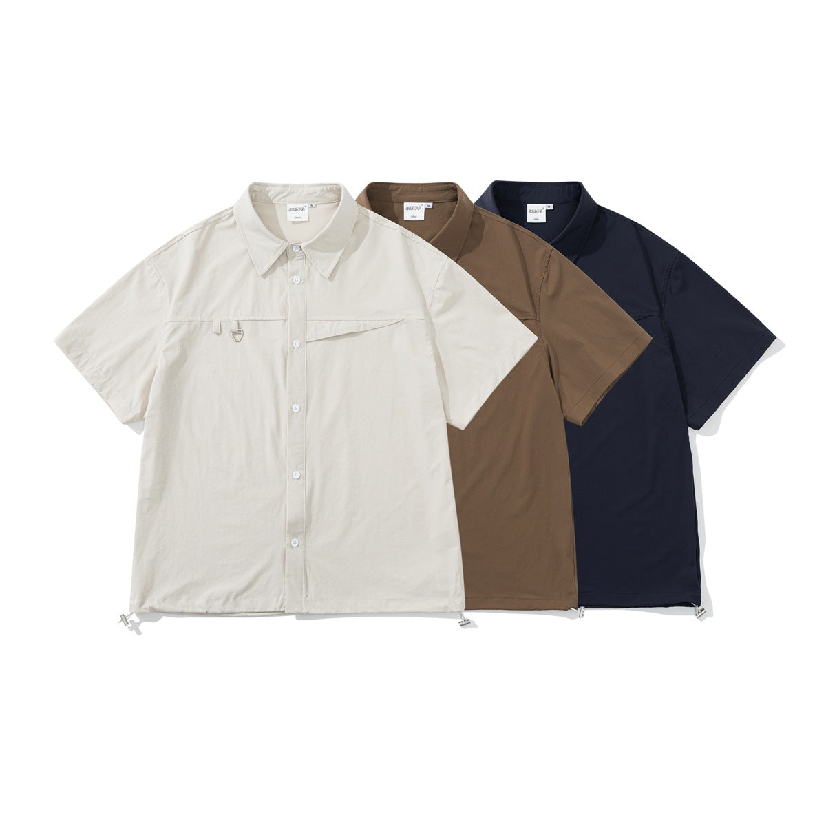 Three short-sleeve button-up shirts shown from the front in cream, brown, and navy.