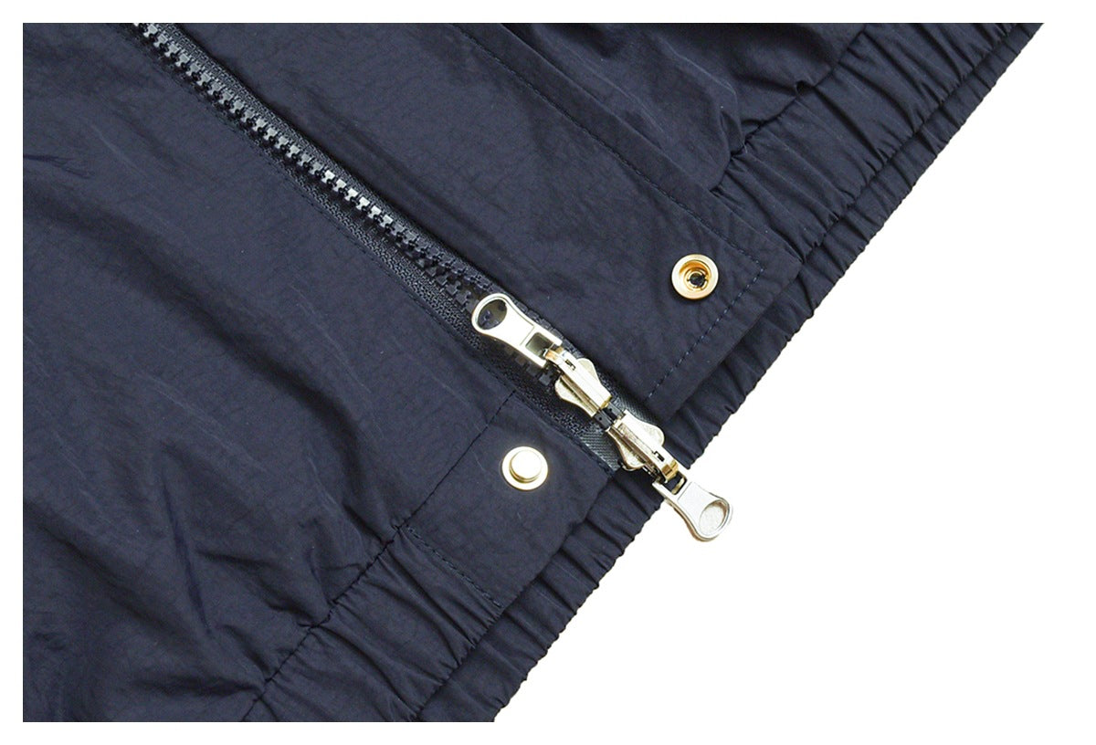 Close-up of a dark jacket zipper, metal pulls, snap fasteners, and gathered elastic edging.