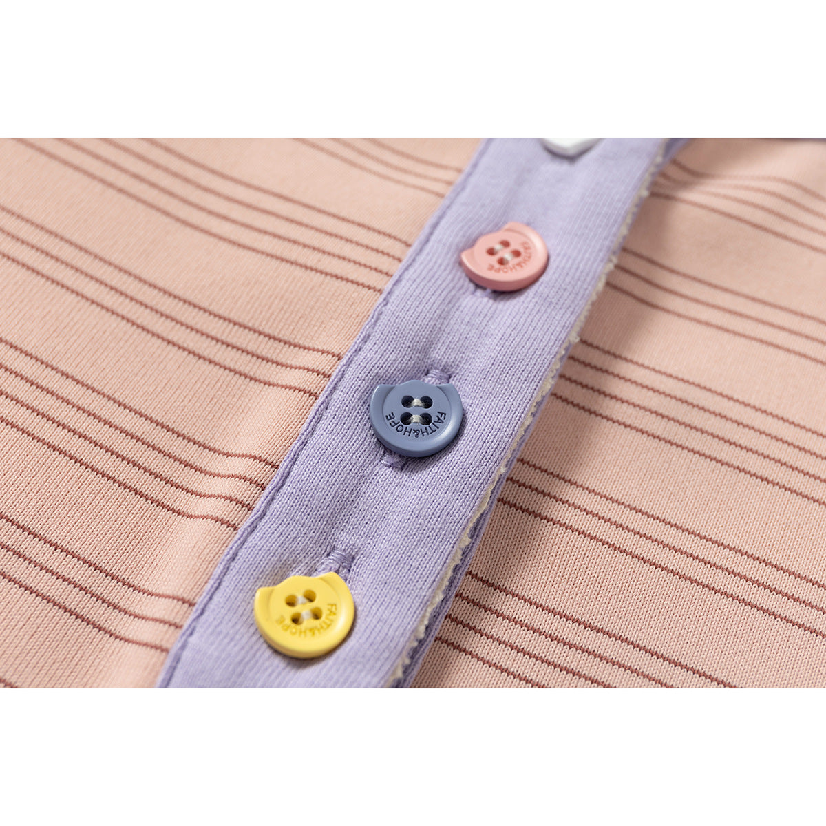 Close-up of a lavender shirt placket with colorful buttons against peach-pink fabric with fine dark stripes.