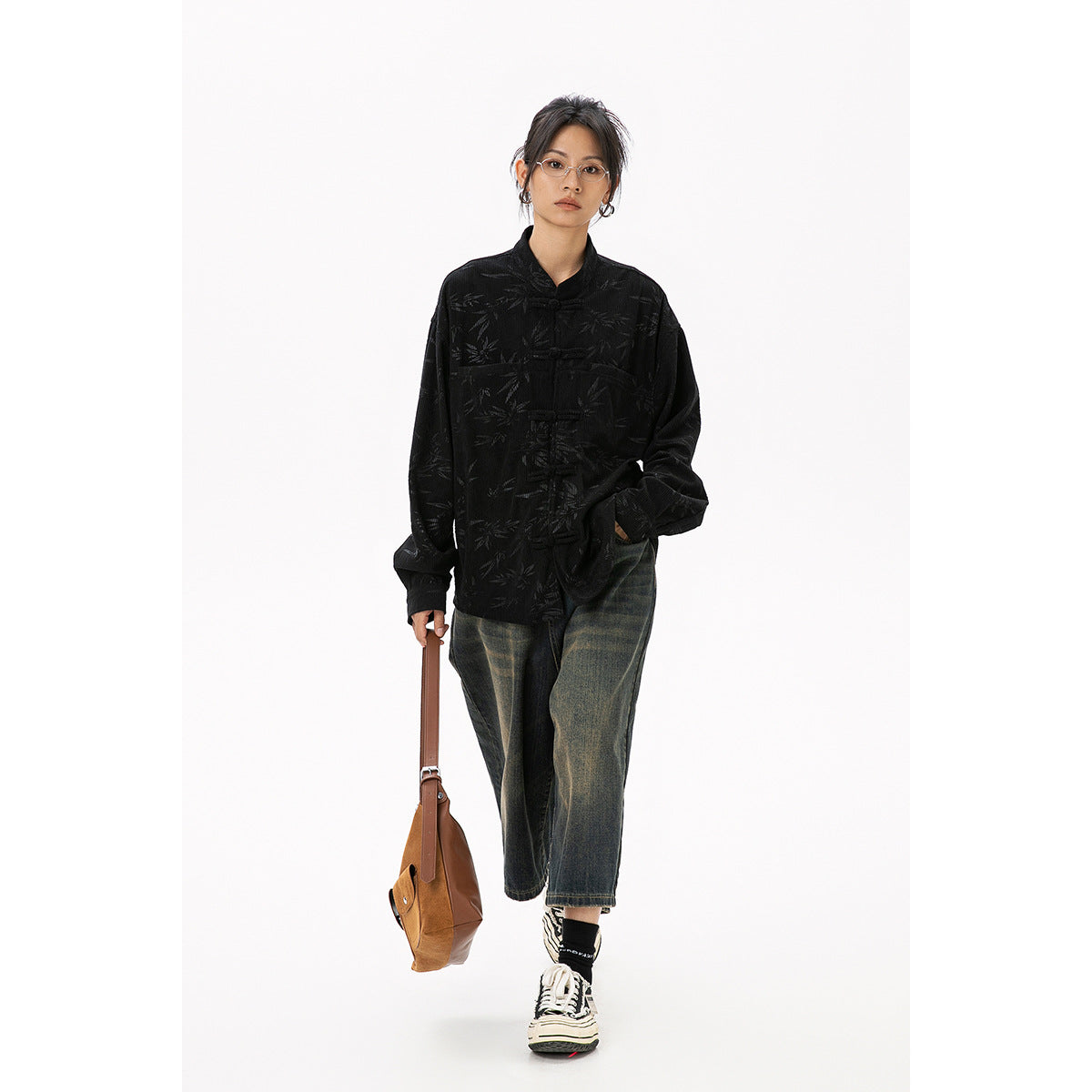 Full-length model wearing a black bamboo-patterned frog-button jacket, cropped jeans, and sneakers.