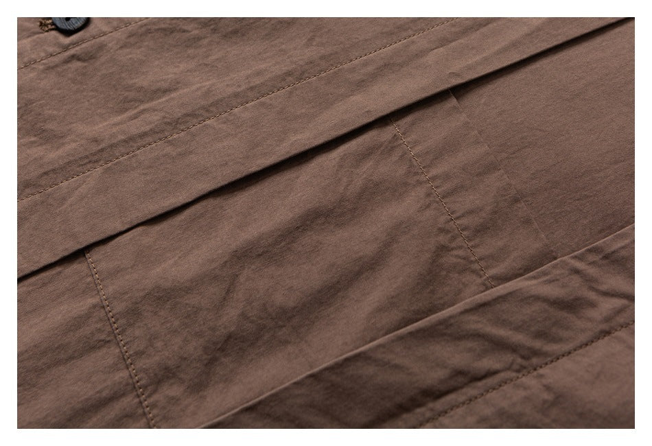 Close-up of brown garment fabric with stitched panels, a folded flap, and part of a dark button.