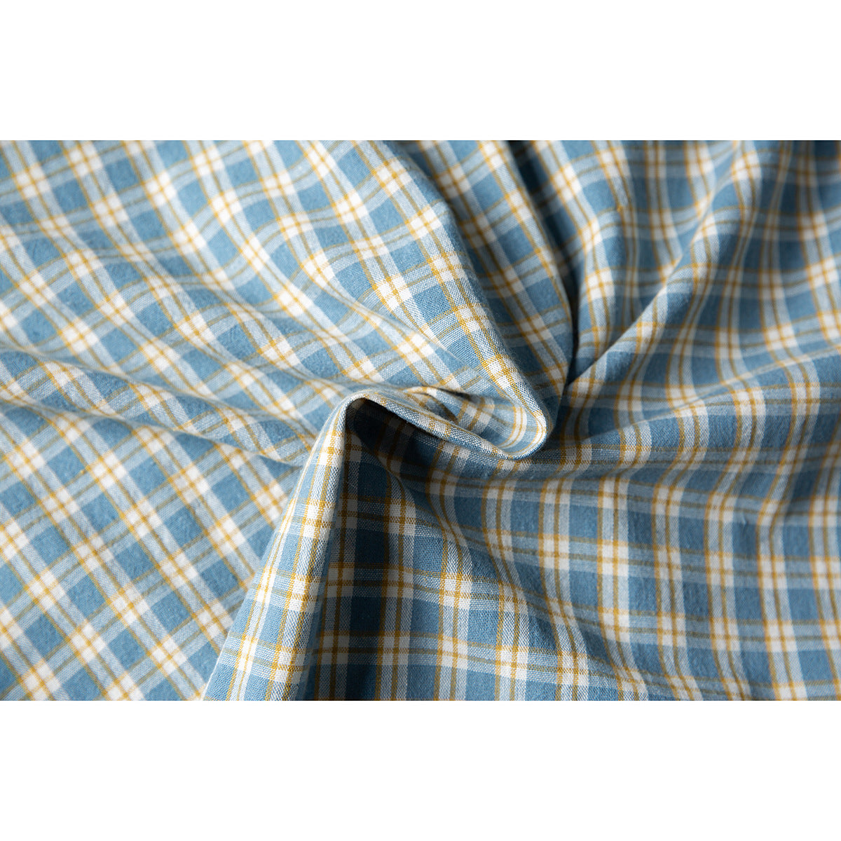 Close-up of blue, white, and mustard plaid fabric gathered into folds, showing its woven check pattern.