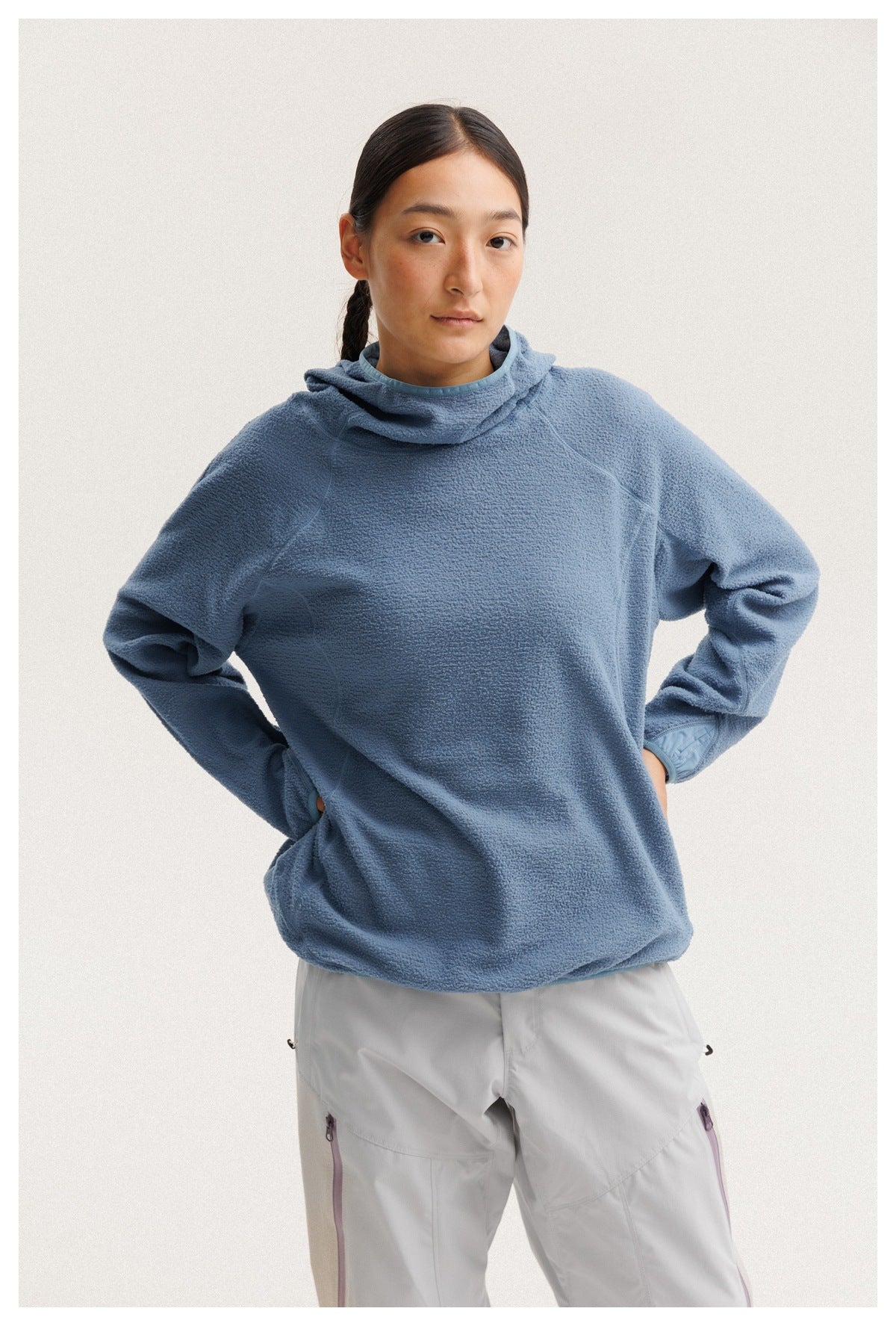 Model wearing a blue cowl-neck fleece pullover with light gray pants, shown from the waist up.