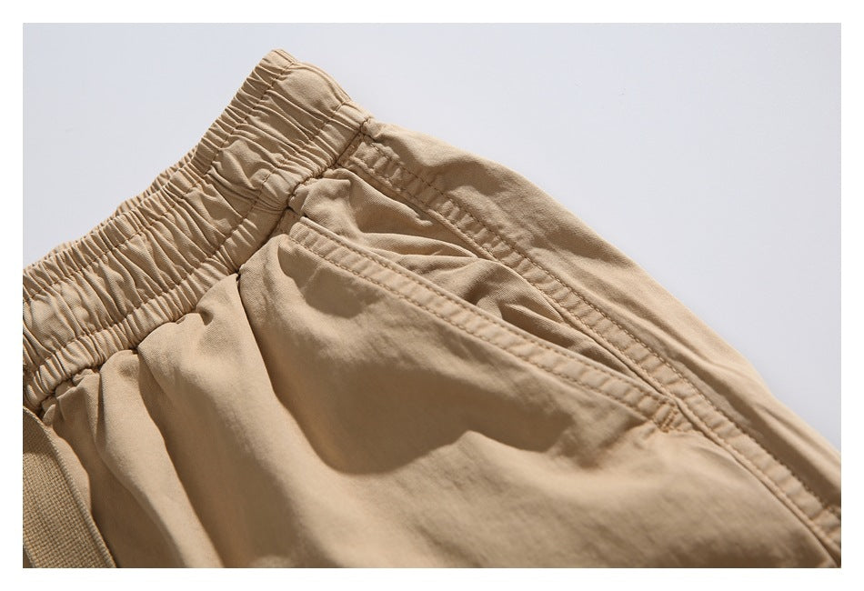Close-up of the tan shorts' elastic waistband and angled front pocket with visible stitching.