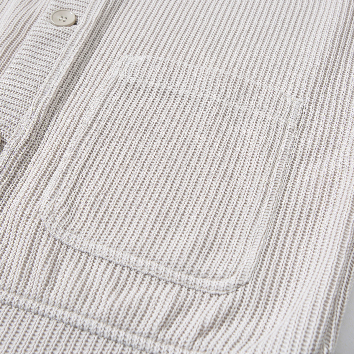 Close-up of the light beige cardigan's ribbed fabric, button placket and patch pocket.