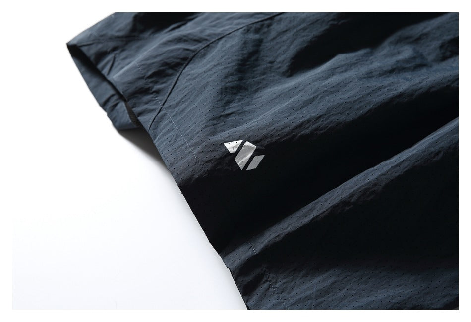 Close-up of black perforated shorts with a small white geometric mark on the leg.