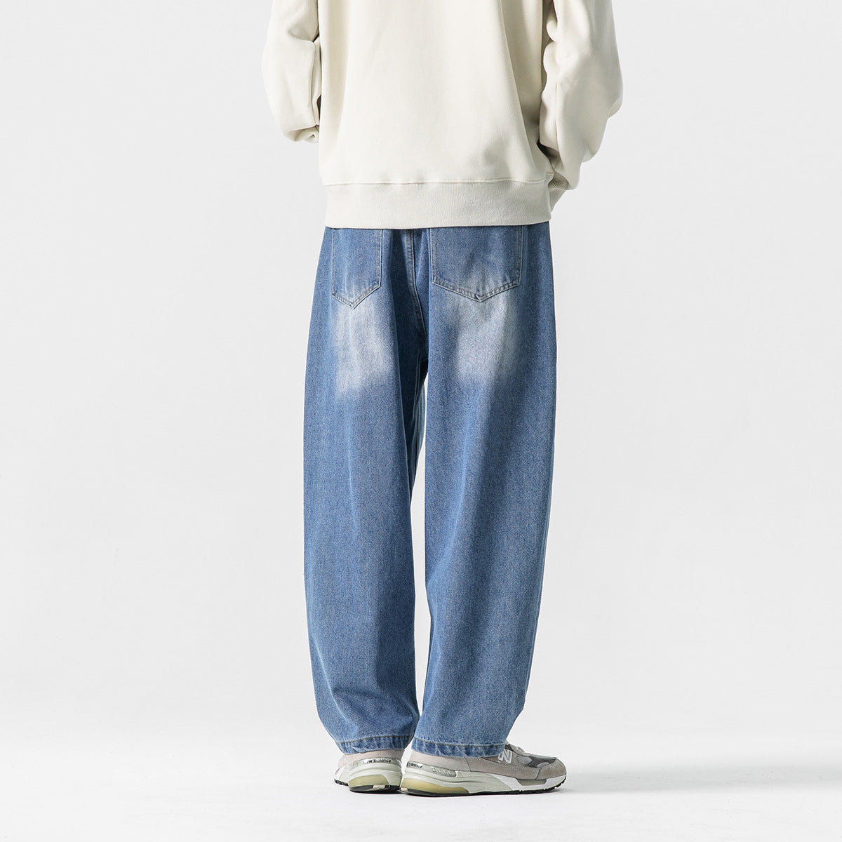 Back view of a model wearing loose blue jeans with two back pockets and a cream sweatshirt.