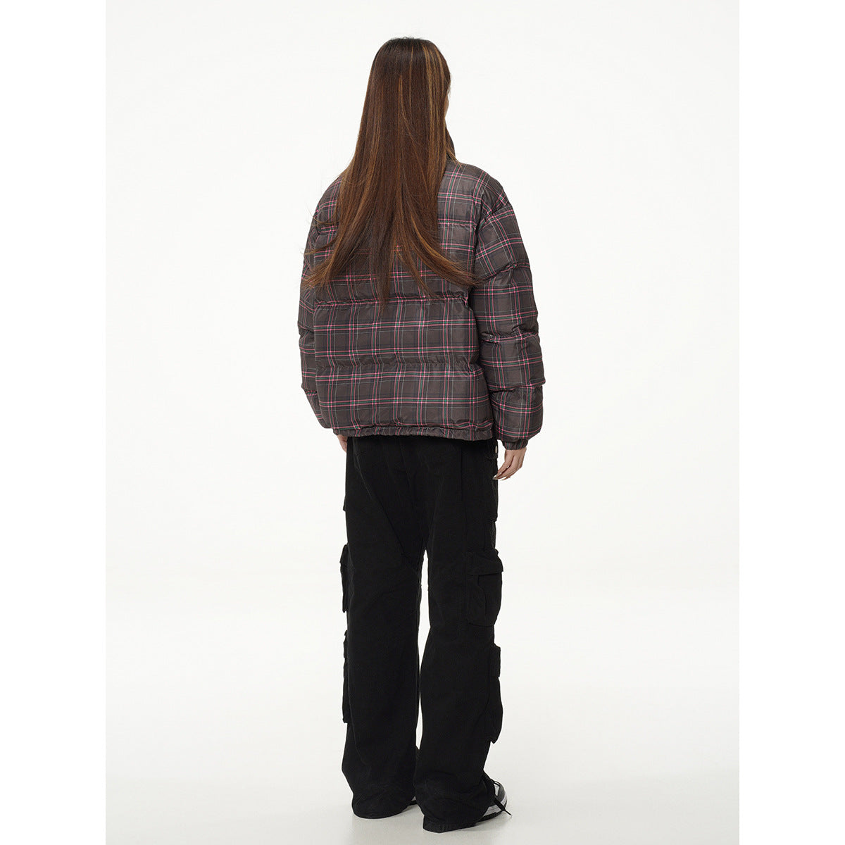 Rear view of a model wearing a dark gray plaid puffer jacket with pink lines and black cargo pants.