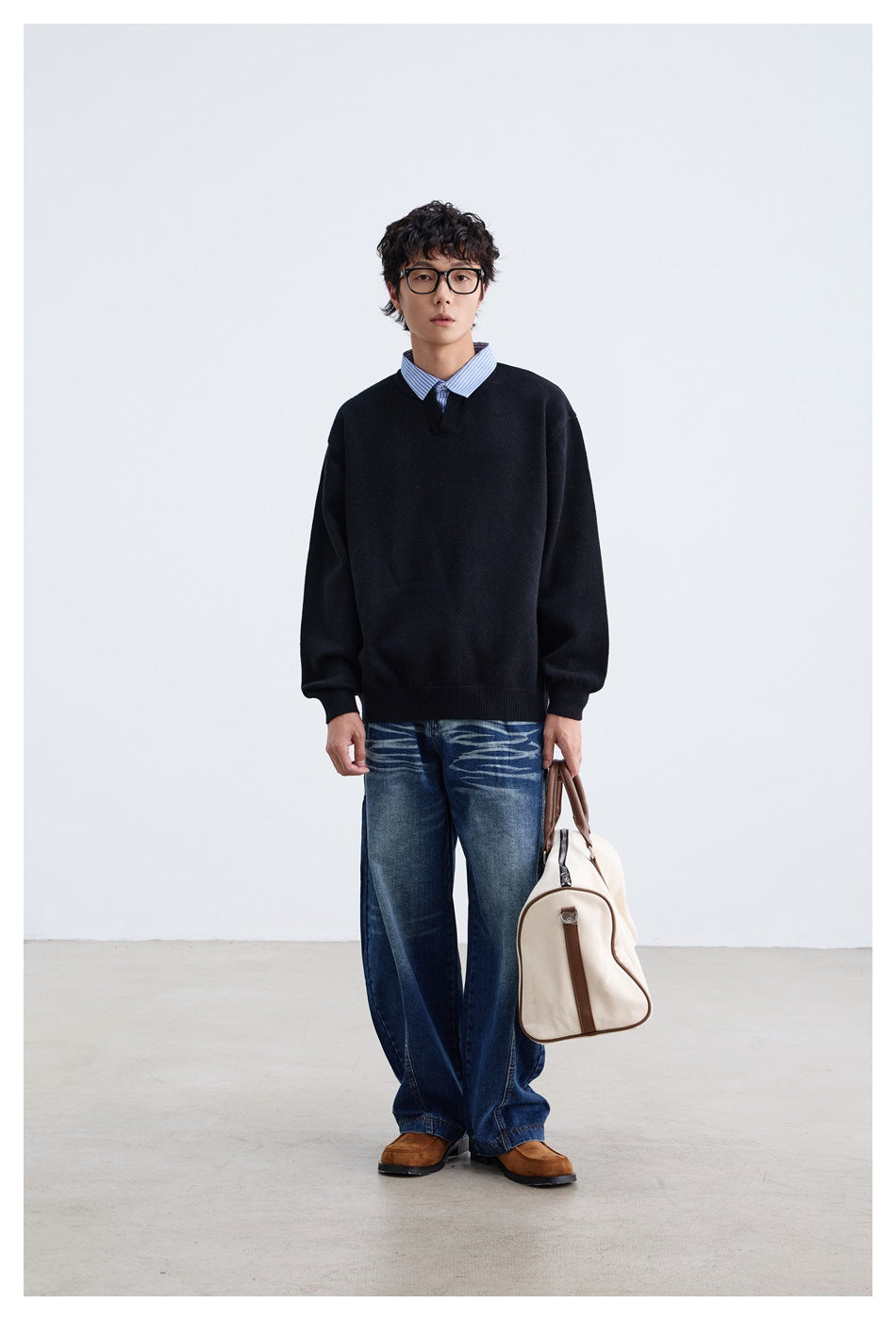 Model wearing a black sweater with striped collar, blue jeans and a canvas duffel bag, front view