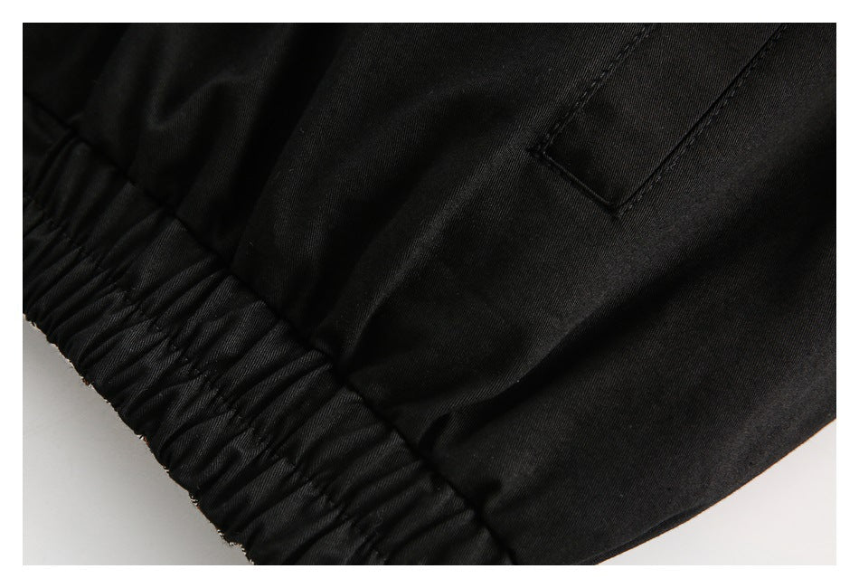Close-up of a gathered elastic hem and pocket detail on black fabric.