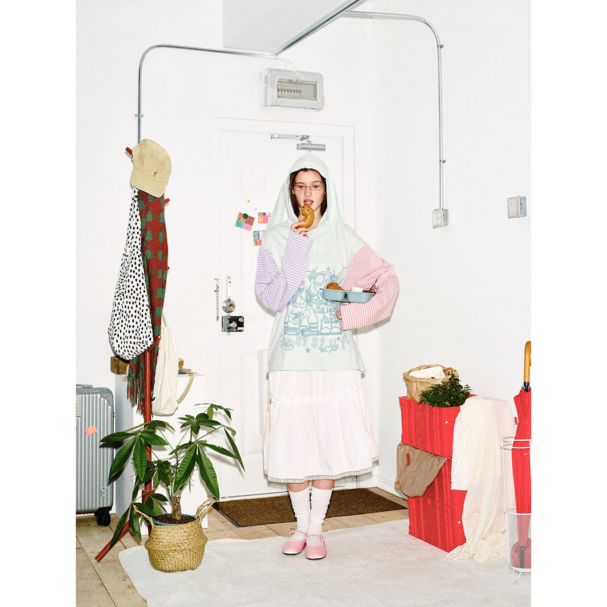 Model in a pale mint graphic hoodie with long hood panels and pink and lilac striped sleeves, holding a snack tray.
