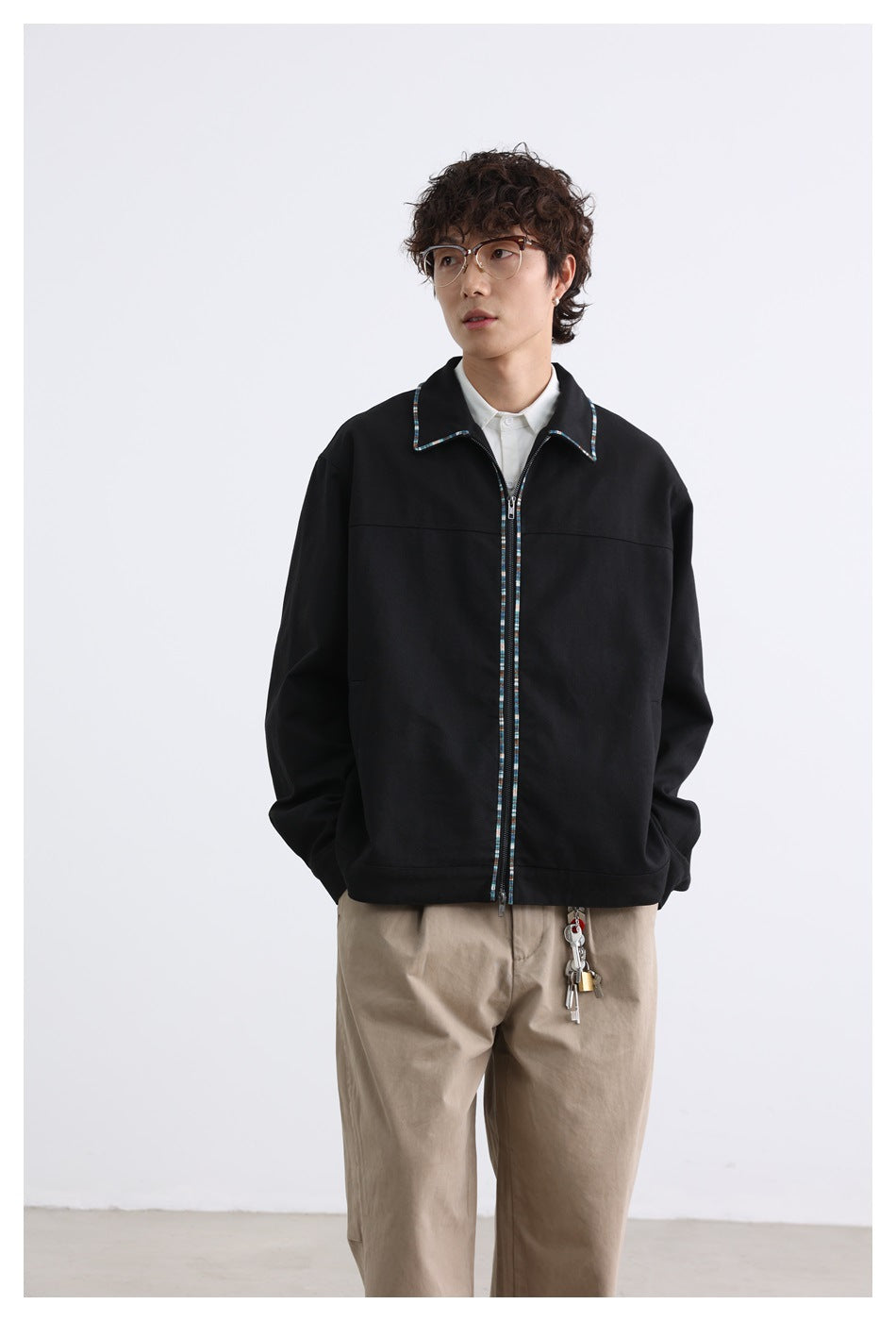 Model wearing a black zip-front jacket with multicolor collar and zipper trim, white shirt and khaki trousers, front view